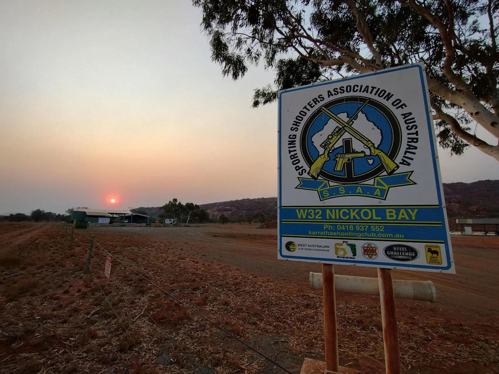The Nickol Bay SSAA range at dusk, with the club sign in the foreground and the Hamersley Ranges on the horizon.
